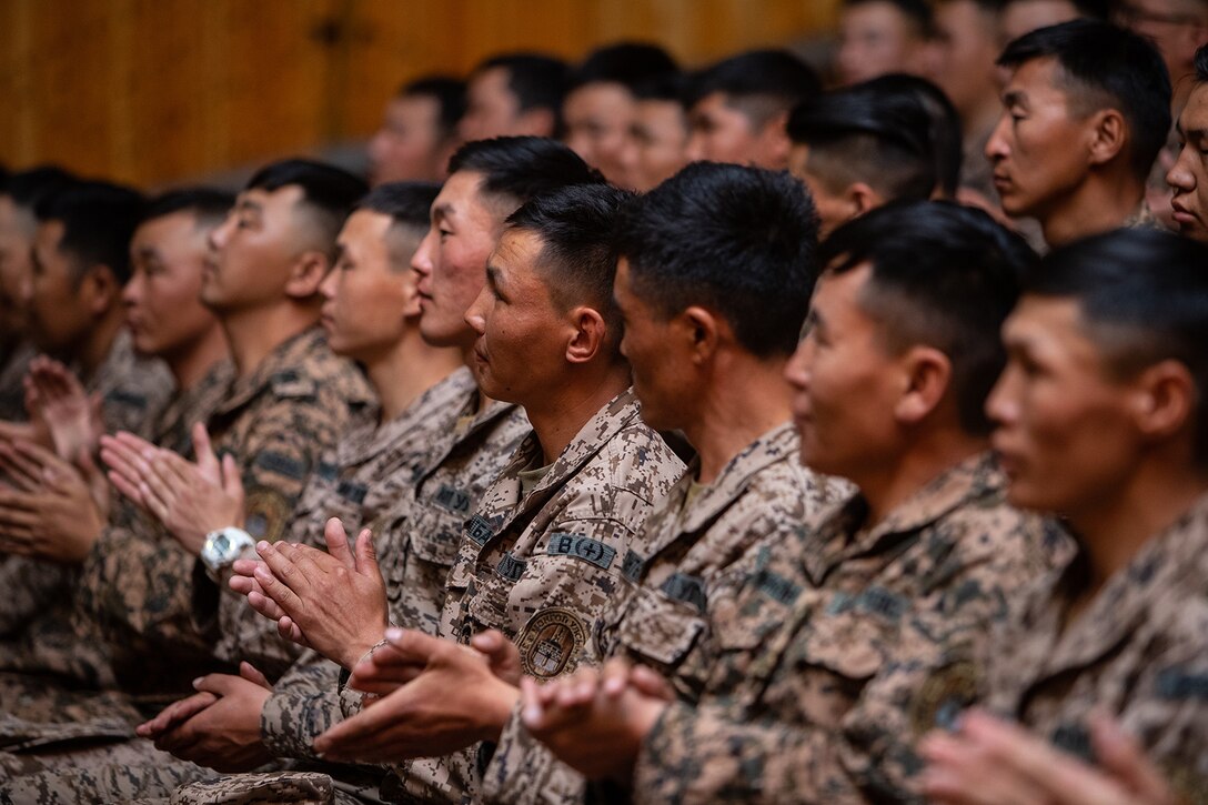 A group of people in military uniforms applaud.
