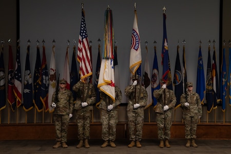 Six members of the color guard stand at attention holding flags and rifles during a ceremony.