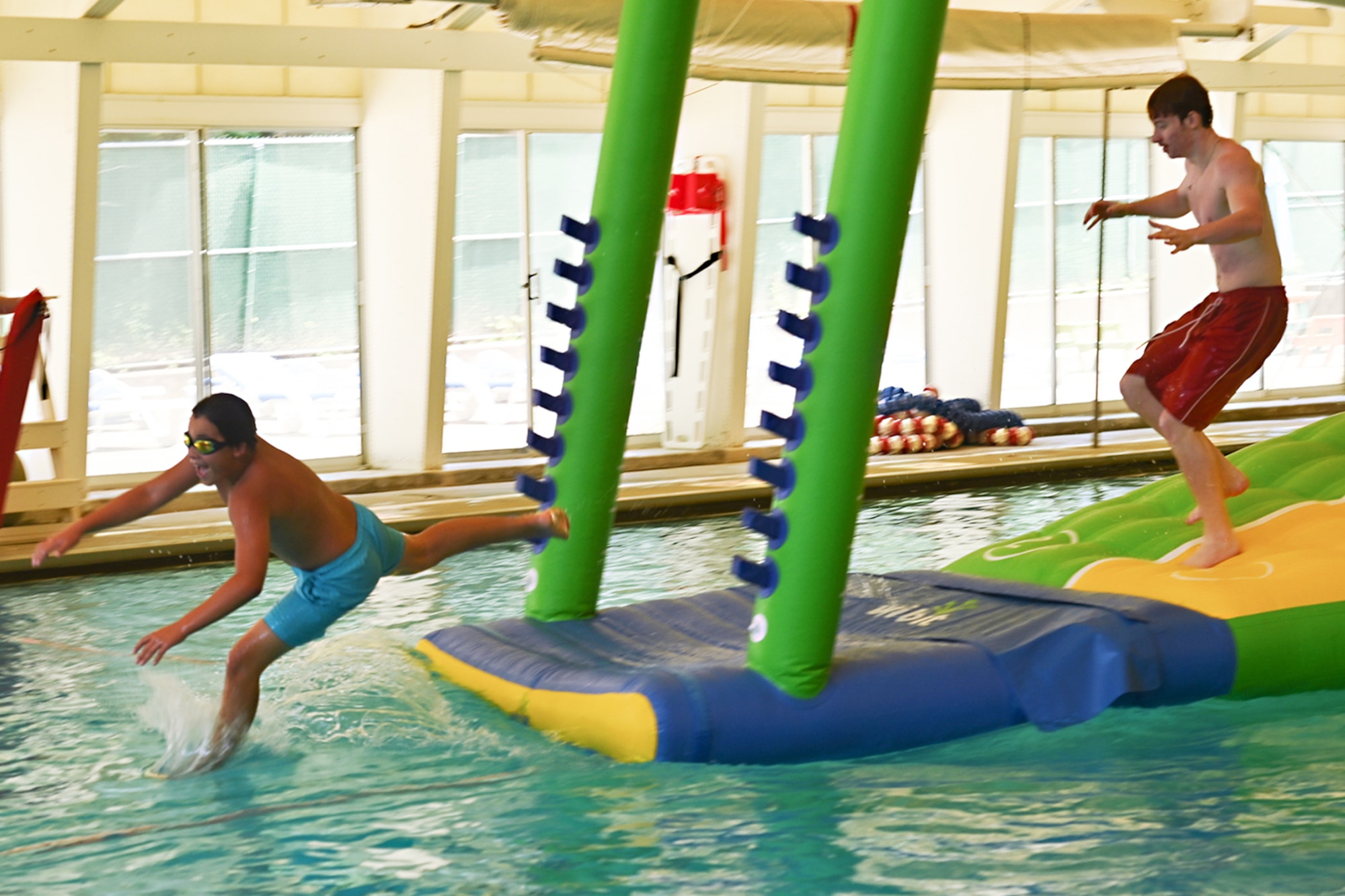 Children jumping off huge inflatable floats in the base swimming pool