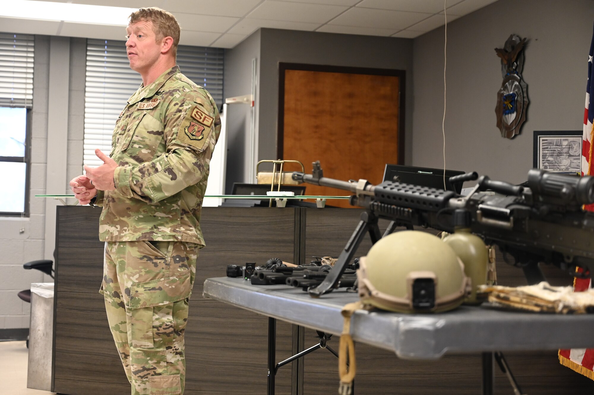 Morris stands in front of table that contains security forces equipment such as helmets and weapons.