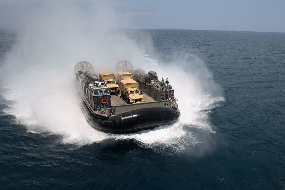 A large cushioned landing craft kicks up spray as it moves in the water.