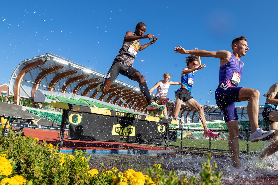 Athletes jump over a hurdle and splash in the water during a race.