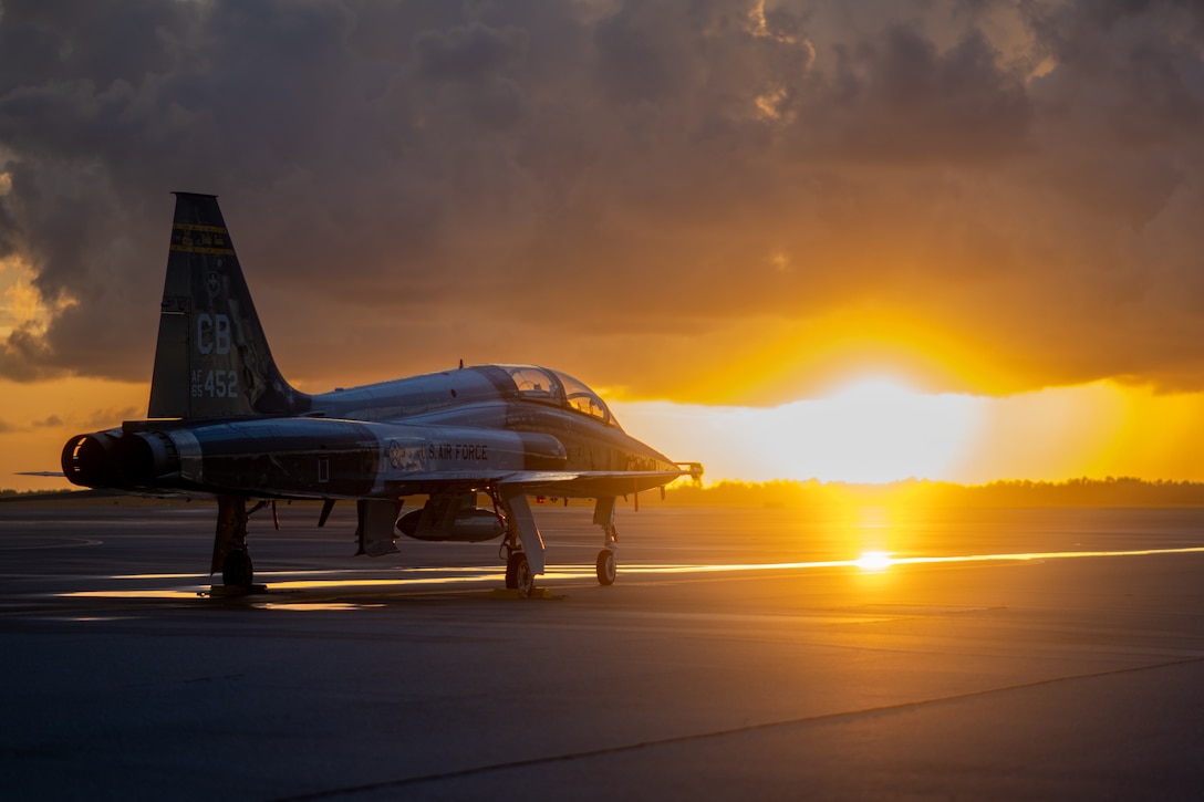 A fighter jet sits on the  tarmac at sunset.