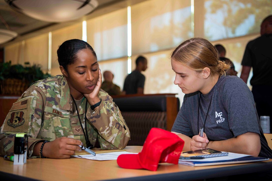 An airman sits at a table next to a cadet candidate while looking over papers.