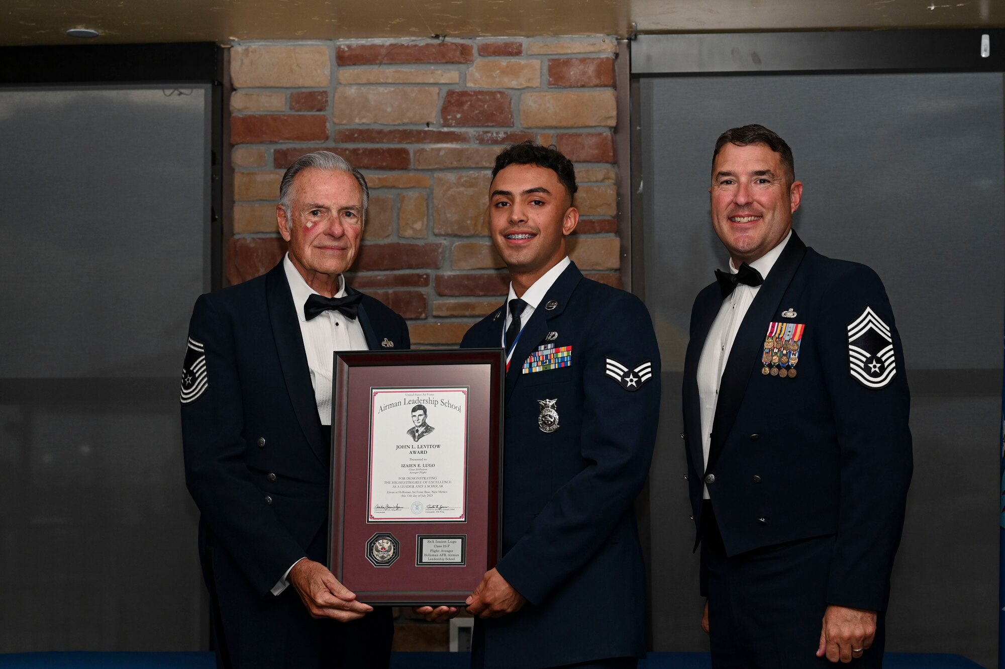 U.S. Air Force Senior Airman Izaien Lugo, Airman Leadership School graduate, middle, receives the John L. Levitow award during the graduation of ALS class 23-F at Holloman Air Force Base, New Mexico, July 14, 2023. The John L. Levitow award is presented to the student demonstrating the highest level of leadership and scholastic performance and is partially determined by the assignment of points by their peers. (U.S. Air Force photo by Airman 1st Class Isaiah Pedrazzini)