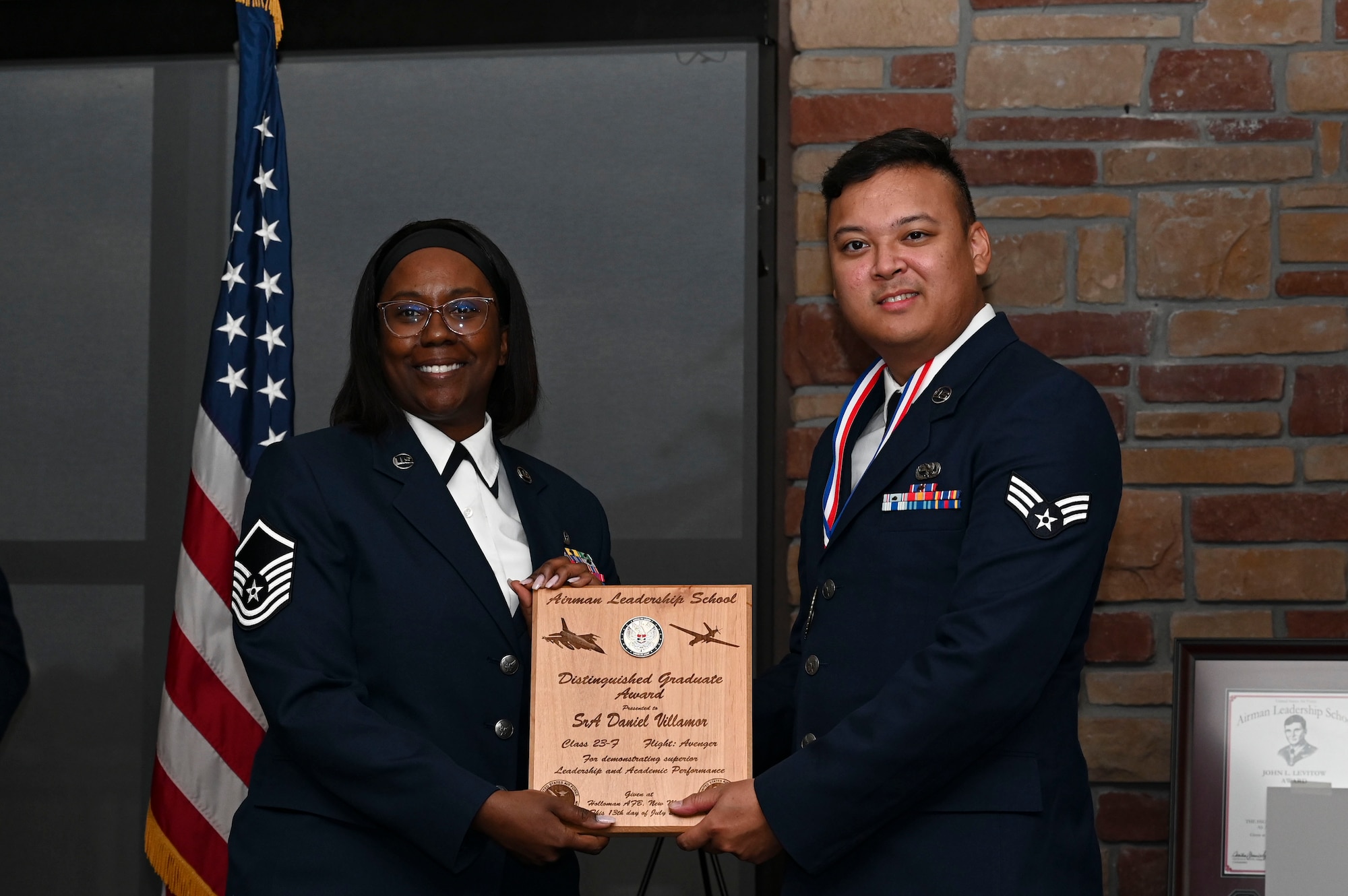 U.S. Air Force Senior Airman Daniel Villamor, Airman Leadership School graduate, right, receives the distinguished graduate Award during the graduation of ALS class 23-F at Holloman Air Force Base, New Mexico, July 14, 2023. The distinguished graduate award is presented to the top ten percent of graduates for their performance in academic evaluations and demonstration of leadership. (U.S. Air Force photo by Airman 1st Class Isaiah Pedrazzini)