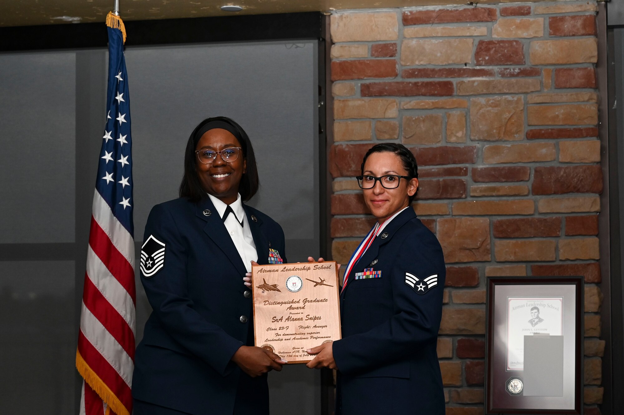 U.S. Air Force Senior Airman Alanna Snipes, Airman Leadership School graduate, right, receives the distinguished graduate Award during the graduation of ALS class 23-F at Holloman Air Force Base, New Mexico, July 14, 2023. The distinguished graduate award is presented to the top ten percent of graduates for their performance in academic evaluations and demonstration of leadership. (U.S. Air Force photo by Airman 1st Class Isaiah Pedrazzini)