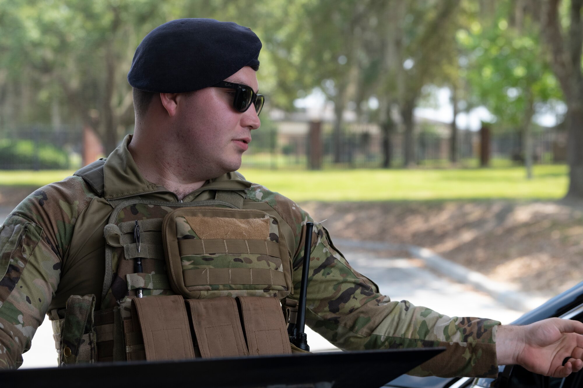 A photo of a uniformed member standing behind a podium outside reaching his hand out to the right of the photo.