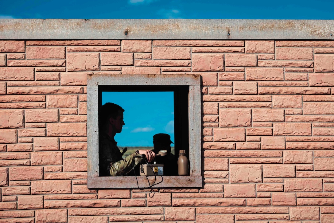 A guardsman shown in silhouette is seen in a window holding onto a piece of equipment.