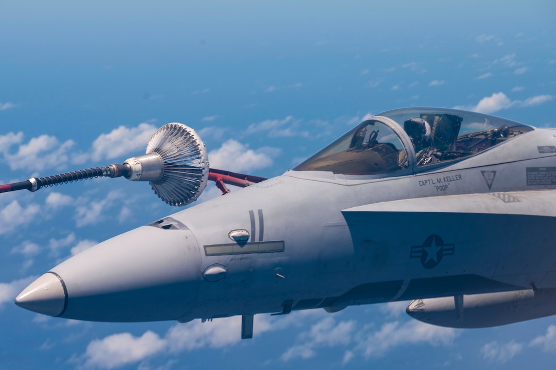 A close-up of an aircraft's boom attaching to another airborne aircraft surrounded by clouds.