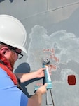 Engineer Bill Manning uses a sealant to prevent water from getting in between the Very High Bond tape on the scupper and the surface of USS Kidd (DDG 100) in Everett, Wash., on June 21, before attaching the 3D-printed overboard discharge scupper. (U.S. Navy photo provided by Dr. Maureen Foley)