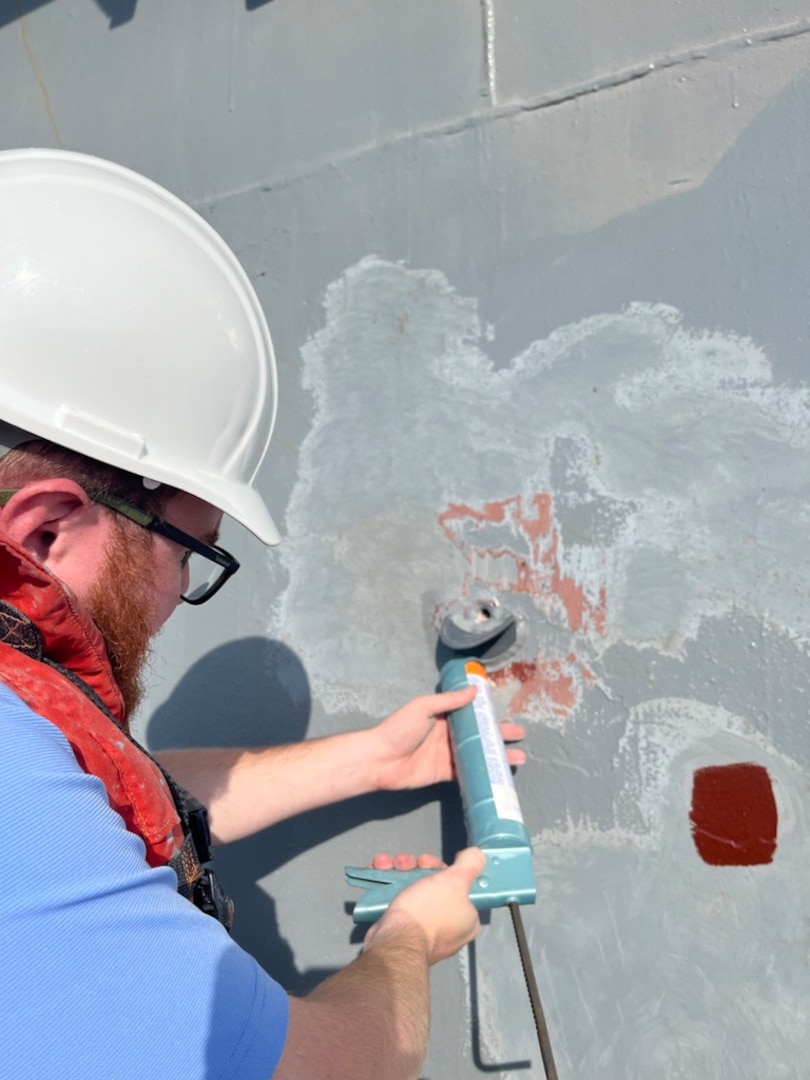 Engineer Bill Manning uses a sealant to prevent water from getting in between the Very High Bond tape on the scupper and the surface of USS Kidd (DDG 100) in Everett, Wash., on June 21, before attaching the 3D-printed overboard discharge scupper. (U.S. Navy photo provided by Dr. Maureen Foley)