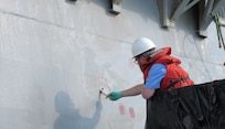 Engineer Bill Manning primes an overboard discharge on the hull of USS Kidd (DDG 100) in Everett, Wash., on June 21, before attaching the 3D-printed overboard discharge scupper. (U.S. Navy photo provided by Dr. Maureen Foley)