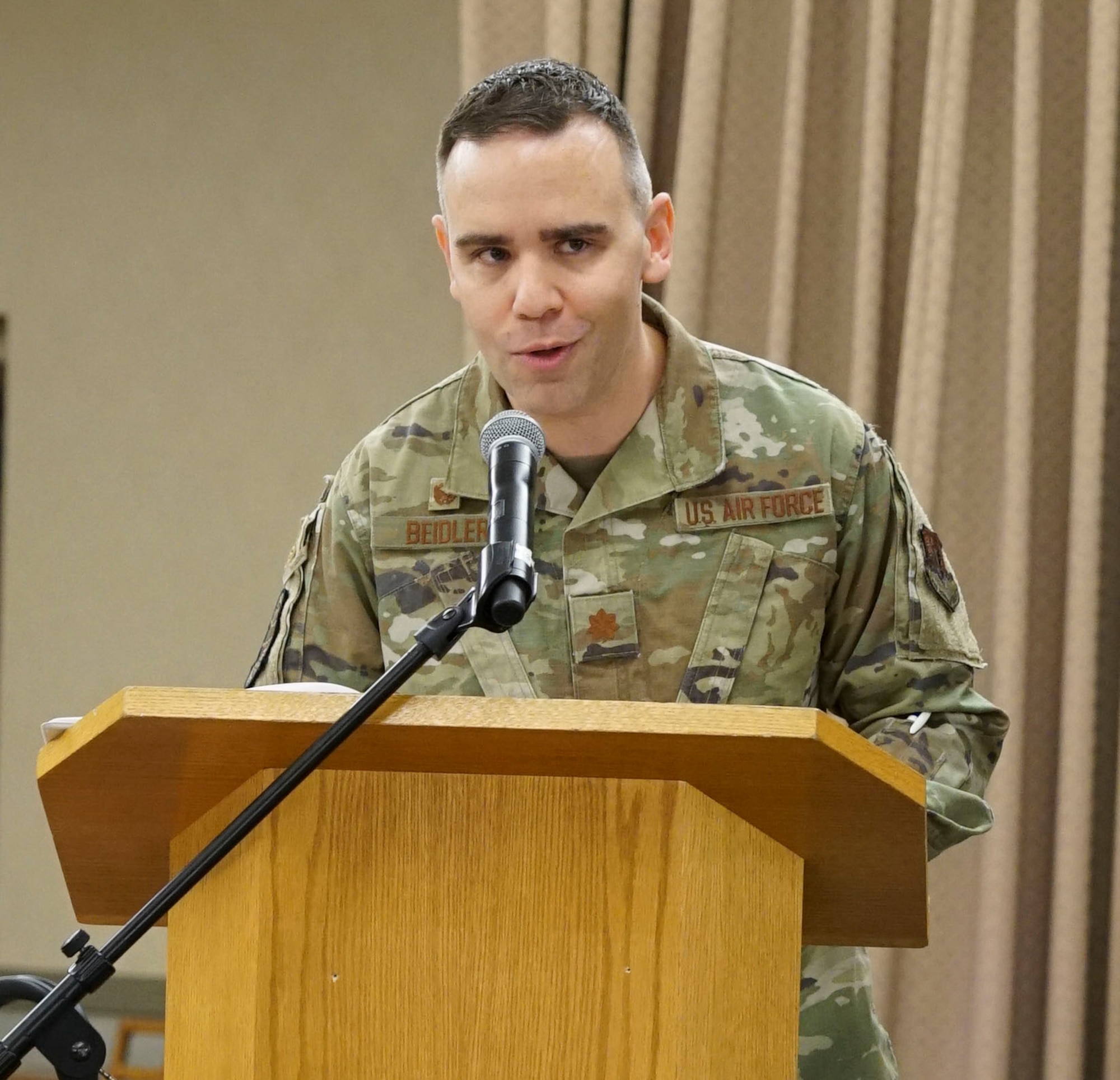 U.S. Air Force Maj. Andrew Beidler gives a speech at a podium.