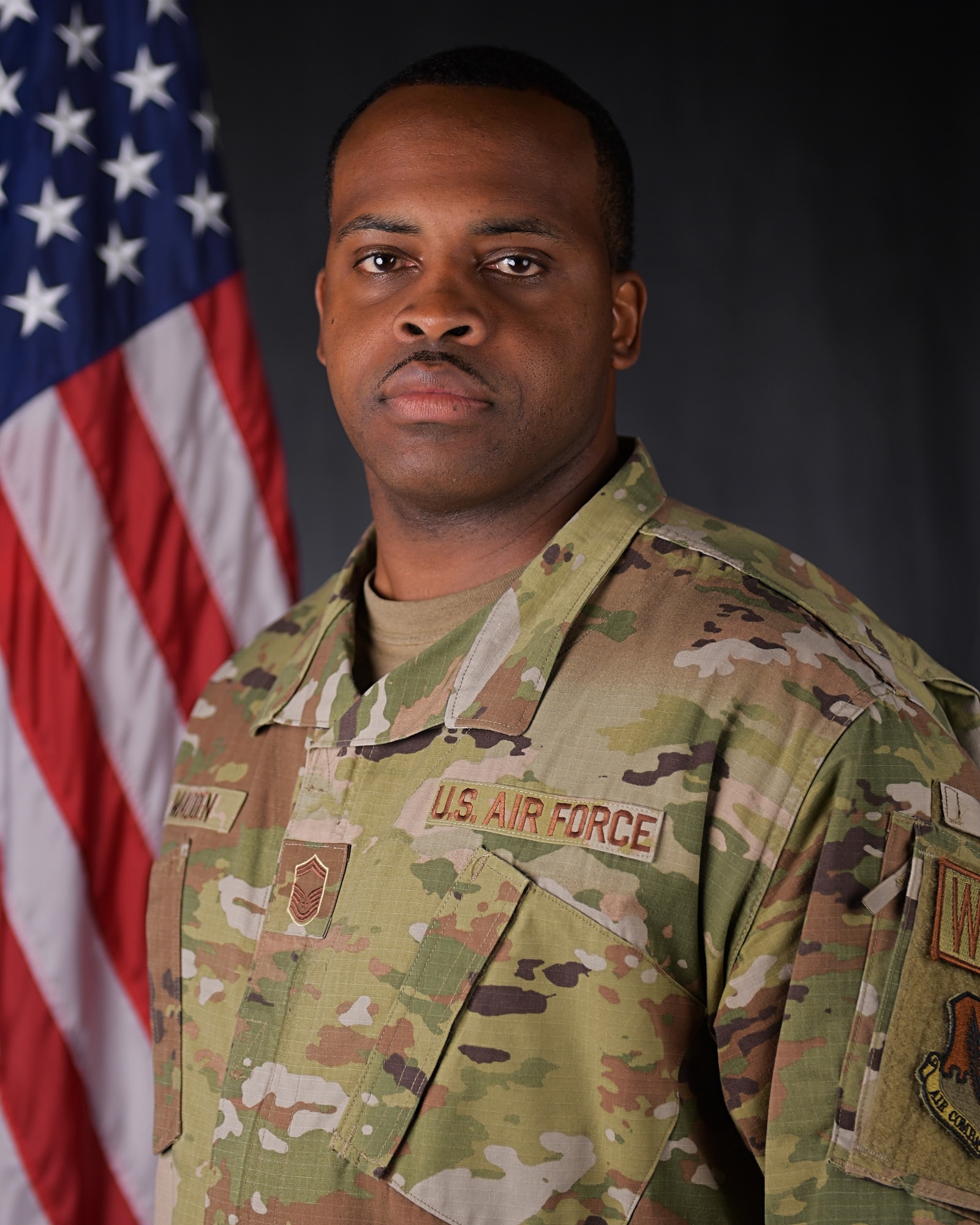 An official photo of someone in OCPs with an American flag in the background.