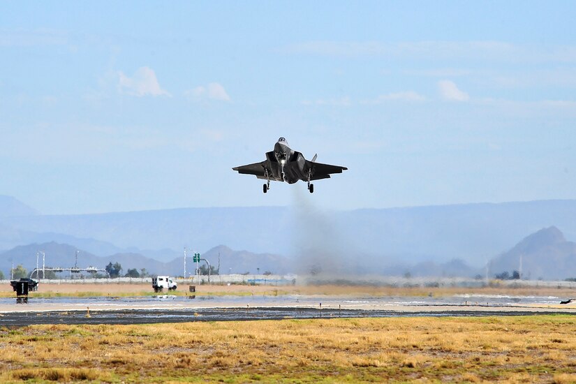 A military fighter is above a runway.