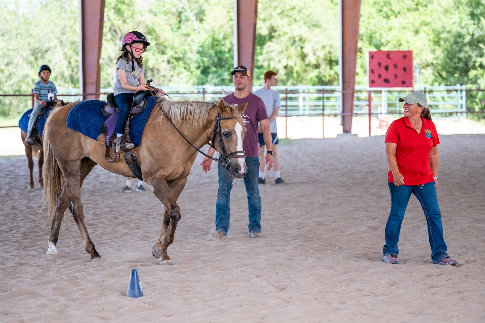 Child rides a horse while her father and instructor watch.