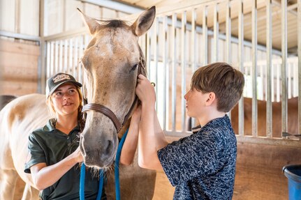 Child attaches lead to a horse while instructor watches.