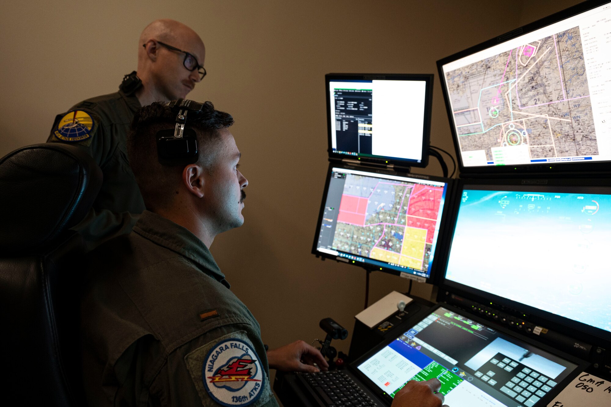 U.S. Air Force Capt. Christopher Carter, 491st Attack Squadron MQ-9 Reaper instructor  pilot, top, prepares to take control of the pilot seat from U.S. Air Force 2nd Lt. Cory Hammond, 136th Attack Squadron MQ-9 student pilot at Hancock Field Air National Guard Base, New York, June 22, 2023. The 491st ATKS is composed of both active duty and Air National Guard personnel responsible for training student pilots and sensor operators on how to fly an MQ-9 Reaper. (U.S. Air Force photo by Airman 1st Class Isaiah Pedrazzini)