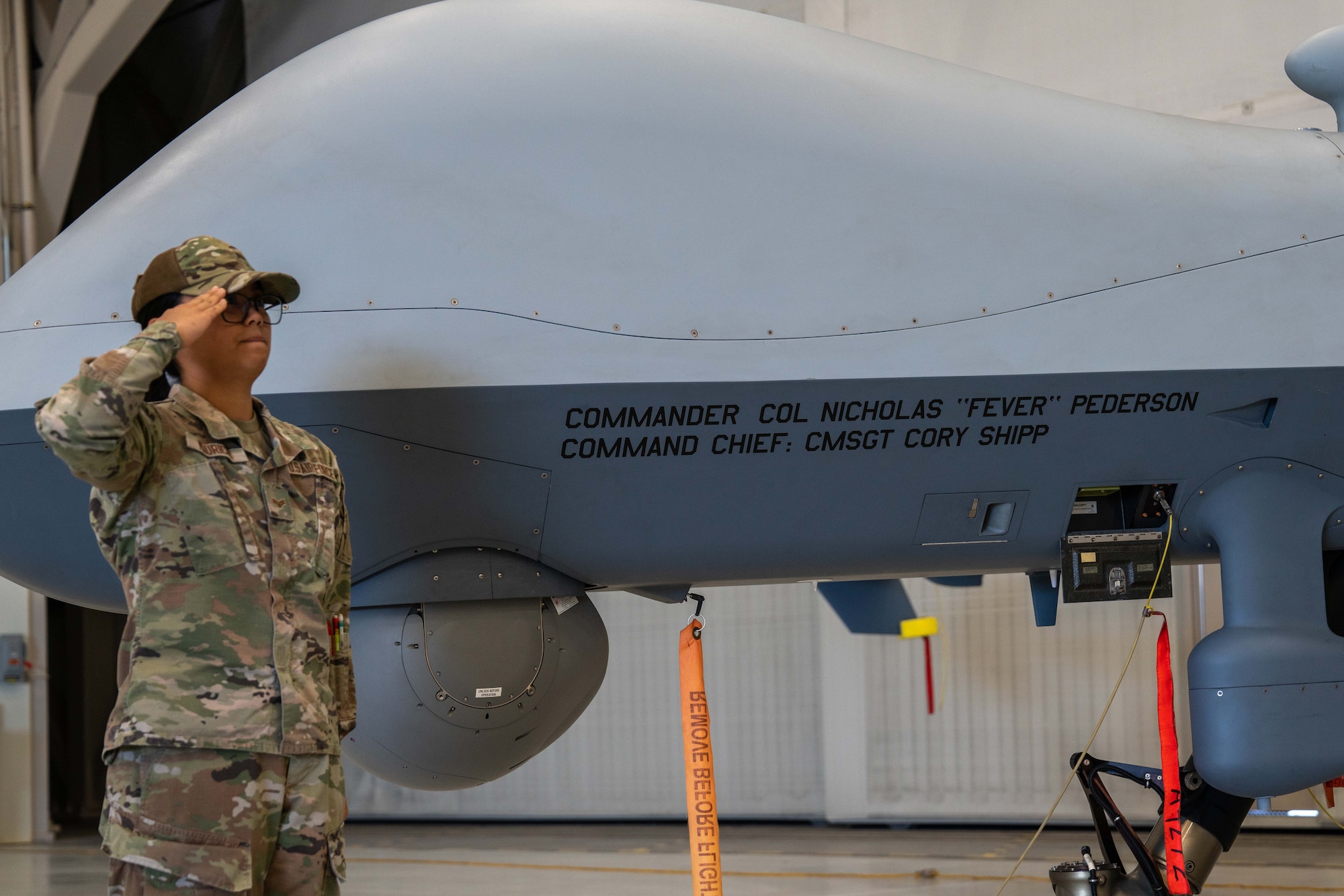 A woman in a military uniform salutes in front of an unmanned aircraft.