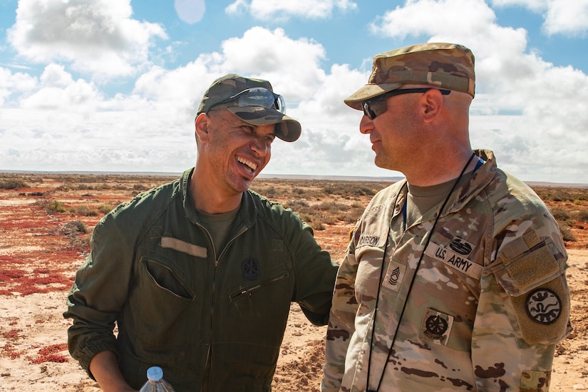 Two men in military uniform laugh with each other.