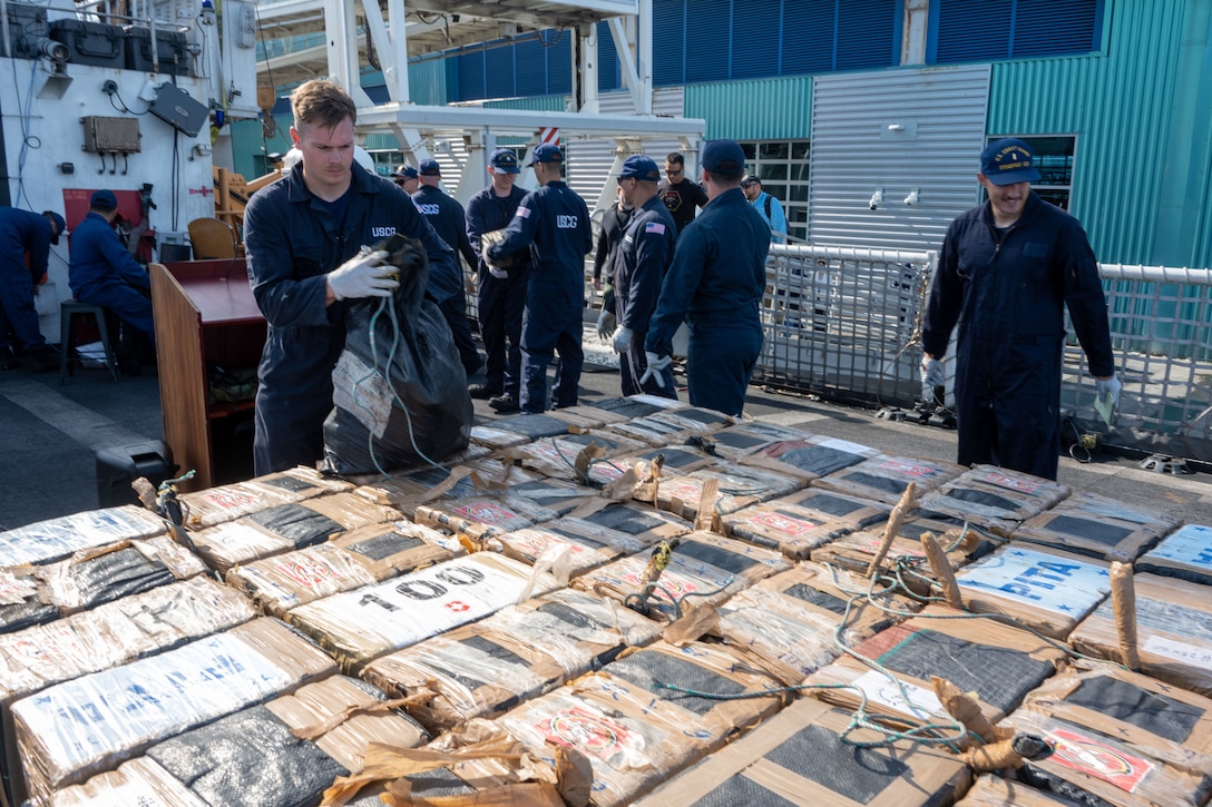 Coast Guard members stack illegal, interdicted drugs on the deck of the cutter.