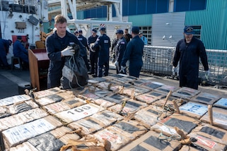 Coast Guard members stack illegal, interdicted drugs on the deck of the cutter.