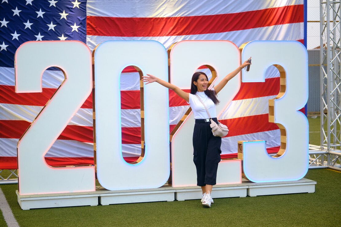 A young woman poses in front of the 2023 marquee at the 4th of July Independence Day Celebration in Yokosuka, Japan.
