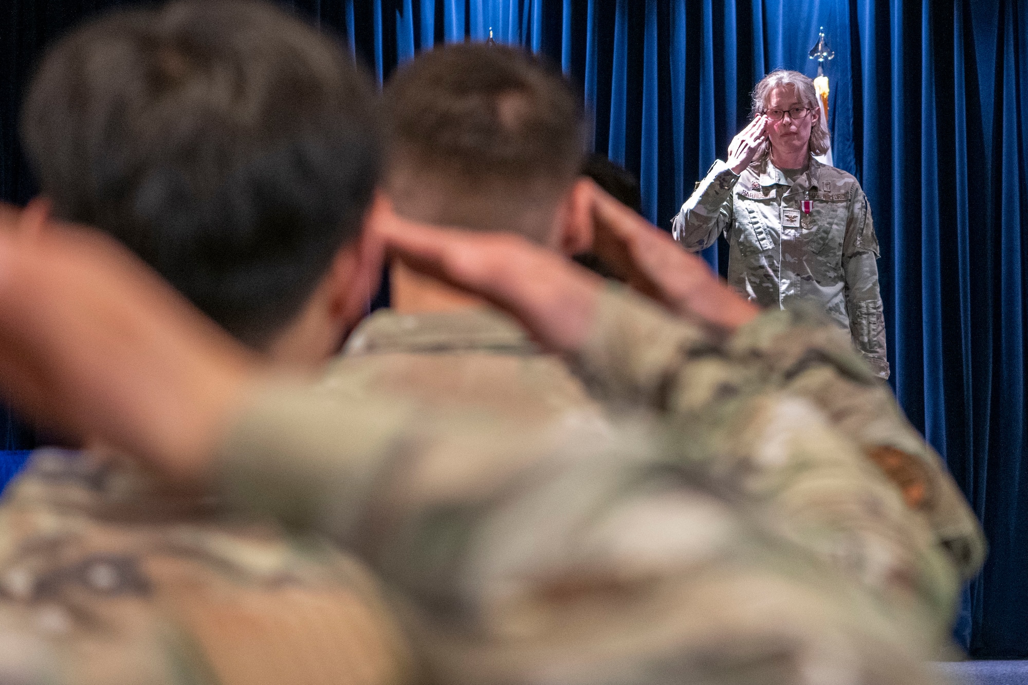 A military woman salutes other military members.