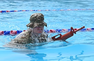 A photo of a man swimming in a pool with a simulated rifle.