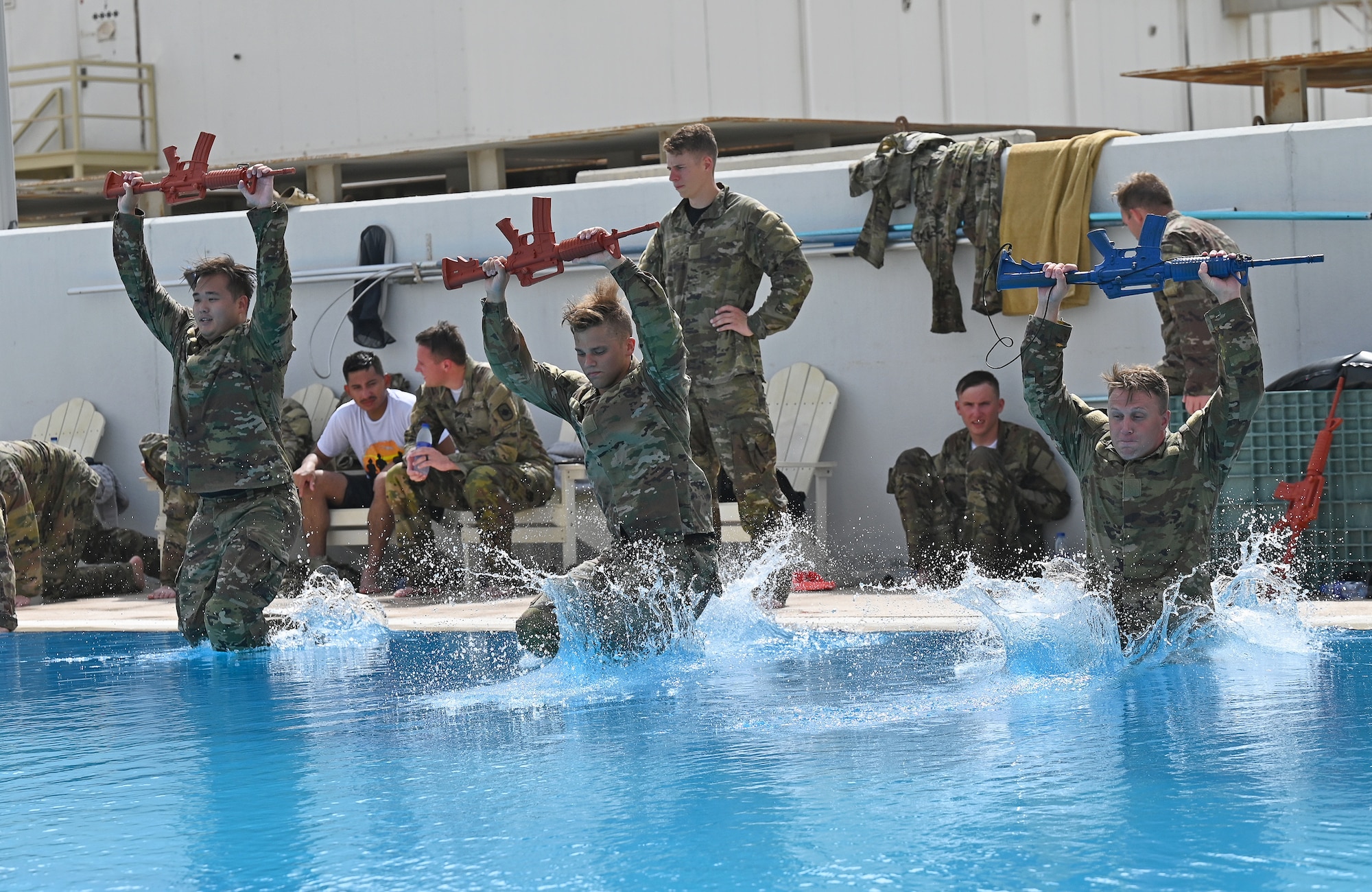 A photo of three of people jumping into a pool with simulated rifles over their heads.