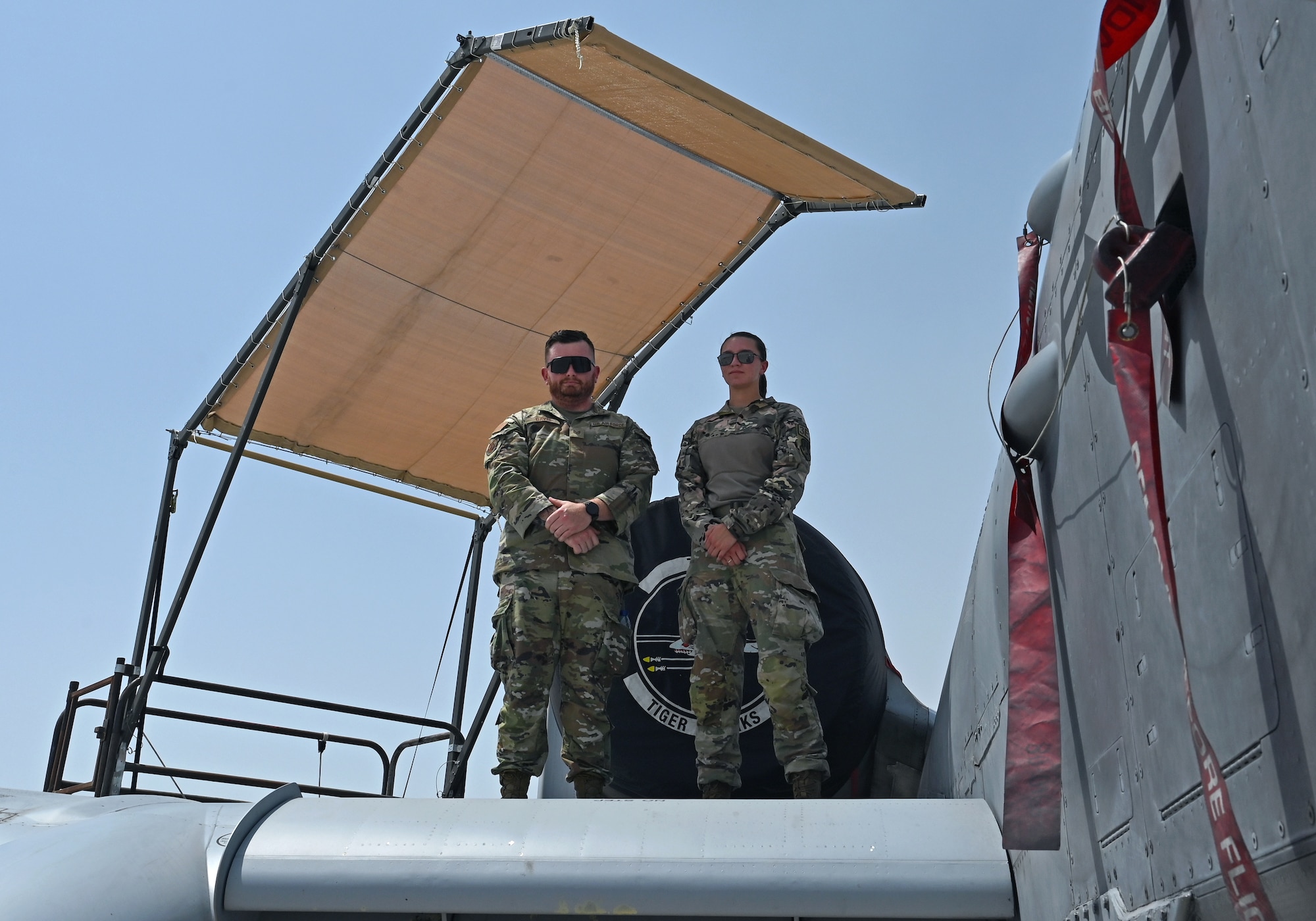 A photo of two people standing on the wing of an aircraft under a sun shade.