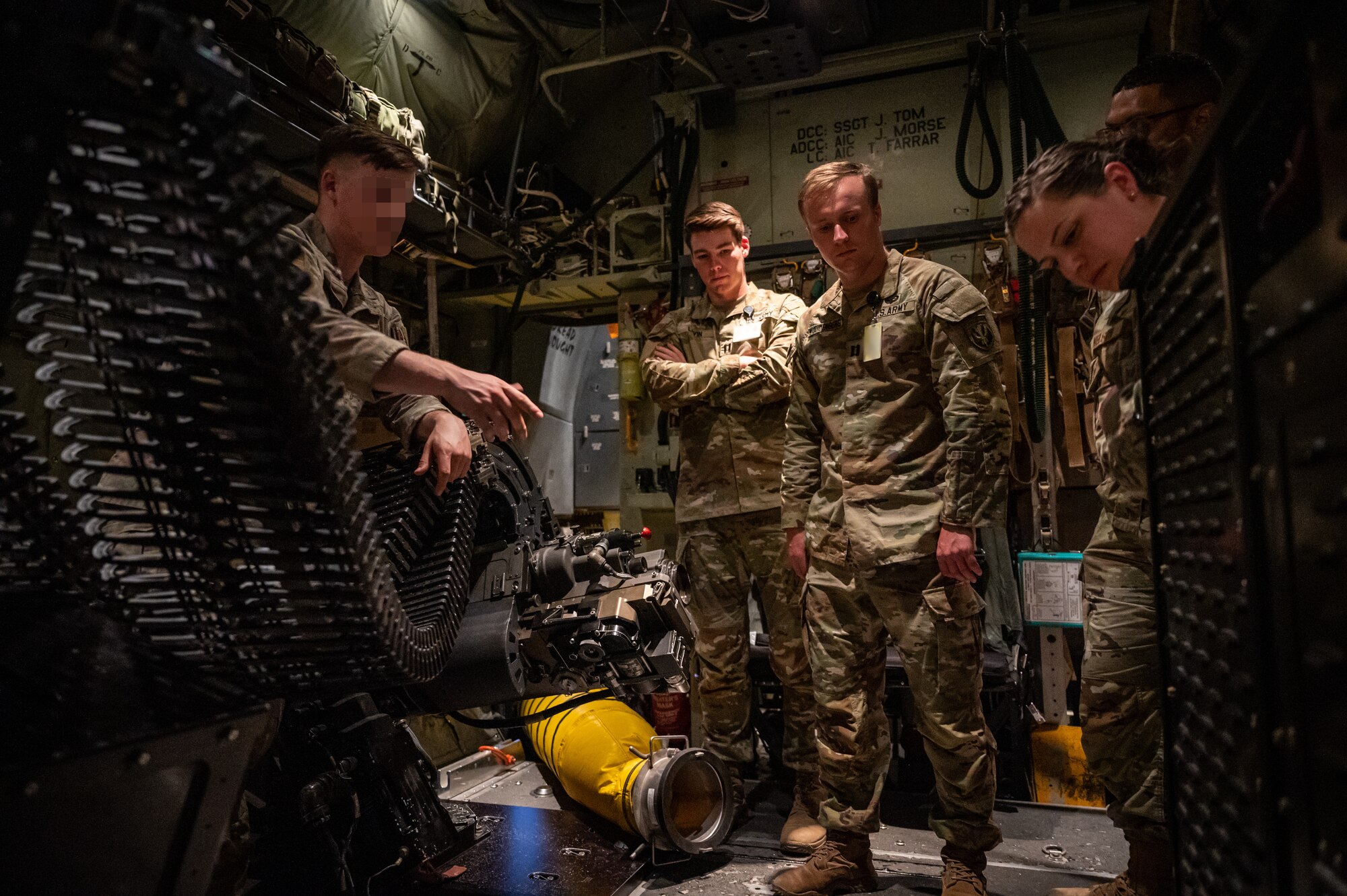 military members in uniform stand around a gun attached to the side of an aircraft.