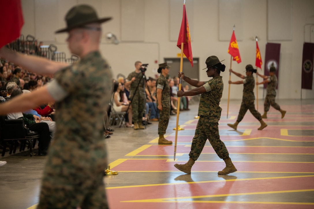 A group of Marines stand in formation holding flags.