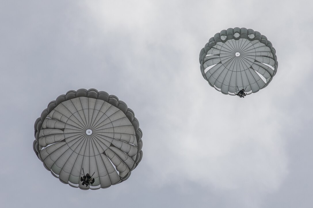 Two soldiers parachute down to the ground.