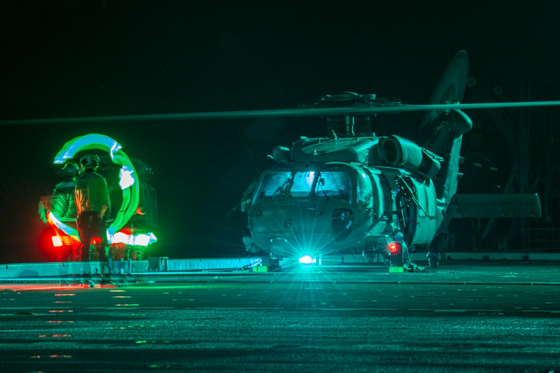 Two sailors signal a helicopter on a ship at night.