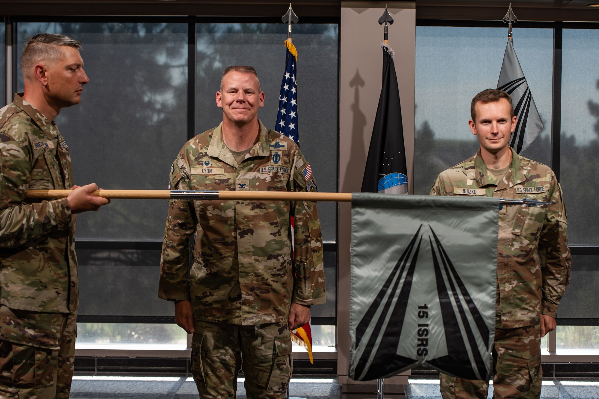 Two men in uniform stand at attention in front of a man in uniform holding a guidon