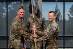 Two men in uniform pass a guidon and smile