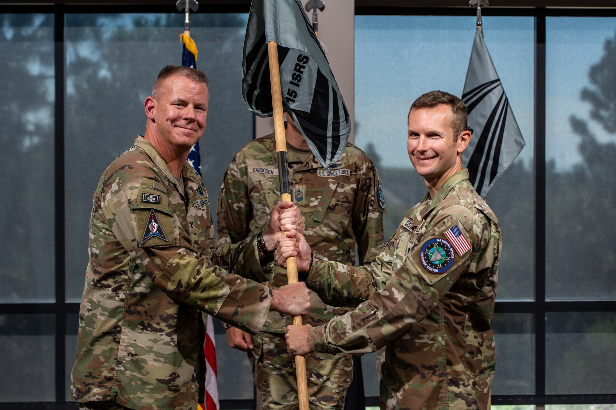 Two men in uniform pass a guidon and smile
