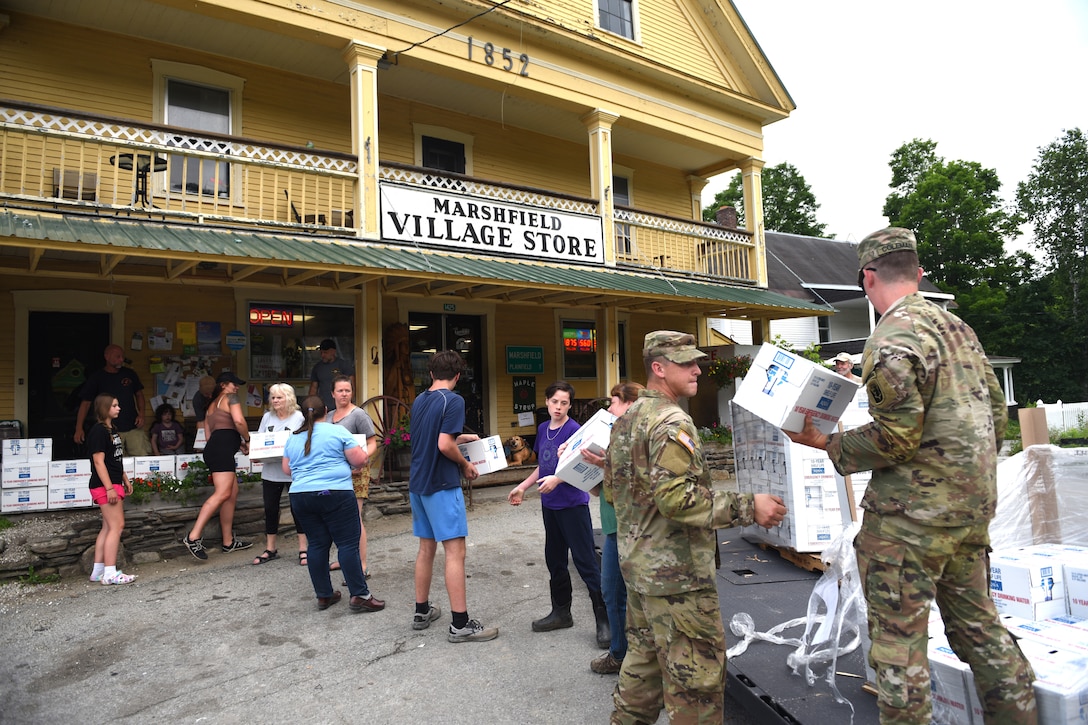 Soldiers unload boxes of water in line for a group of residents in front of a village store.