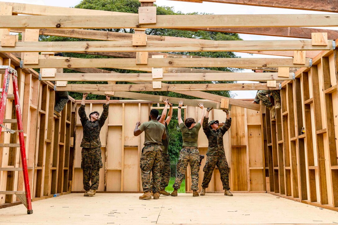 Marines install roof trusses on a building.