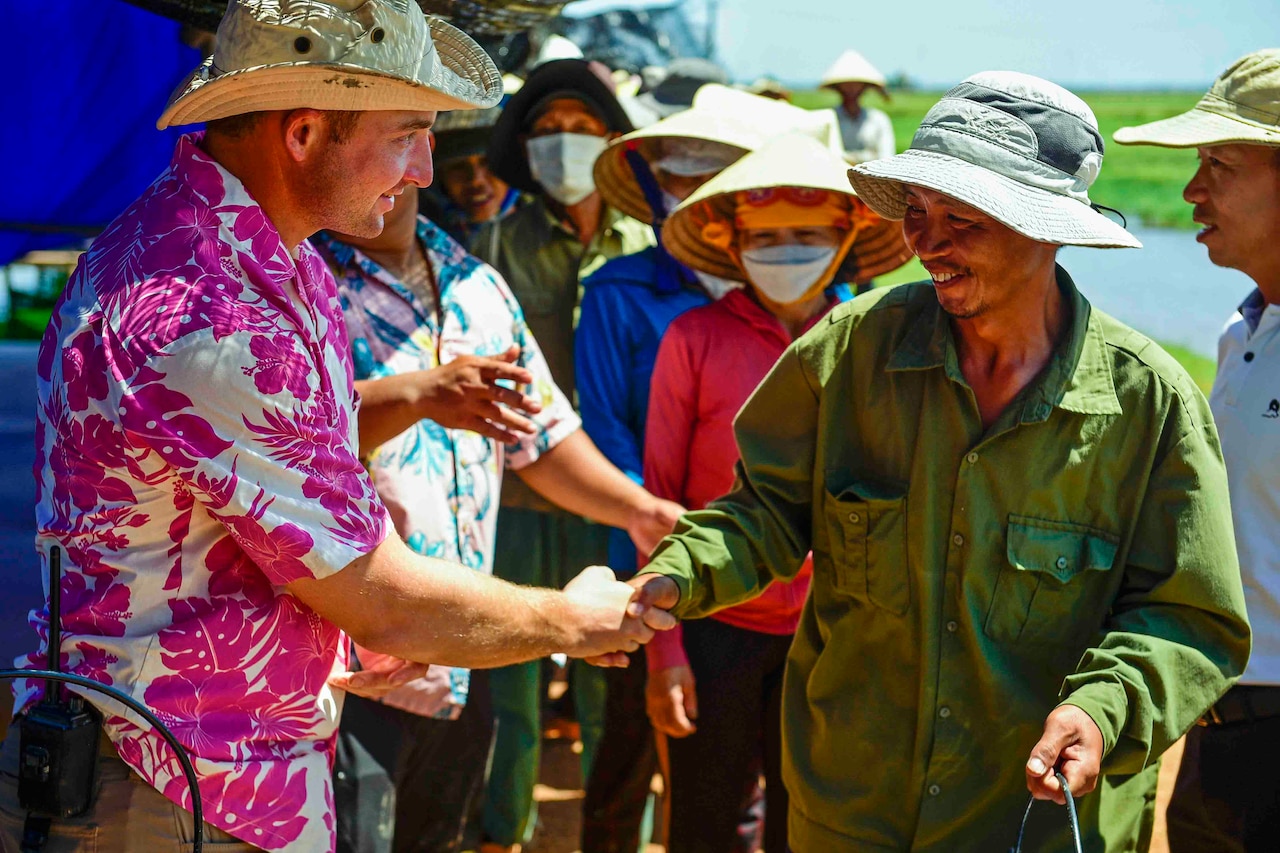 A soldier shakes hands with a person as a group of people stand behind them.