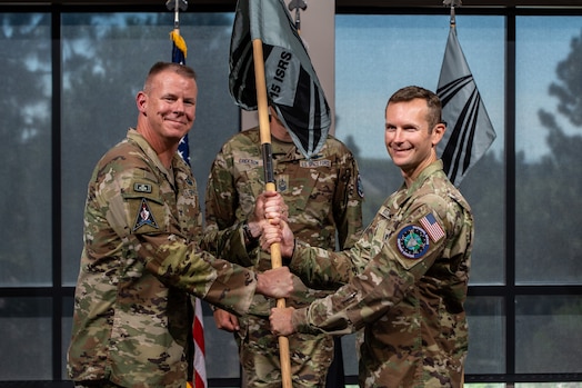  Two men in uniform pass a guidon and smile