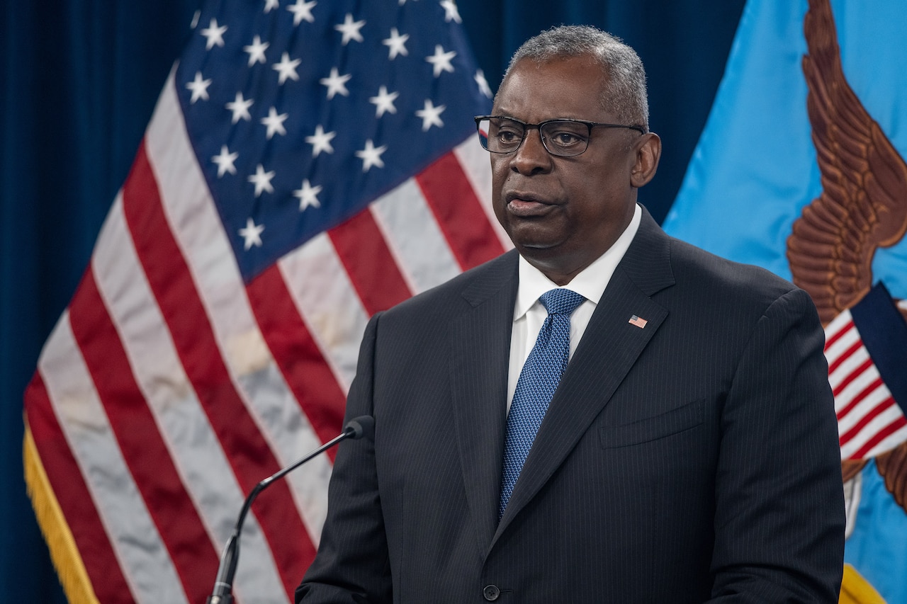 A man stands behind a podium in front of flags.
