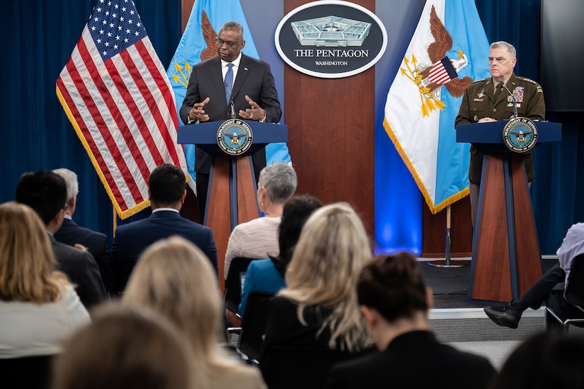 Two men stand behind podiums in front of an audience.