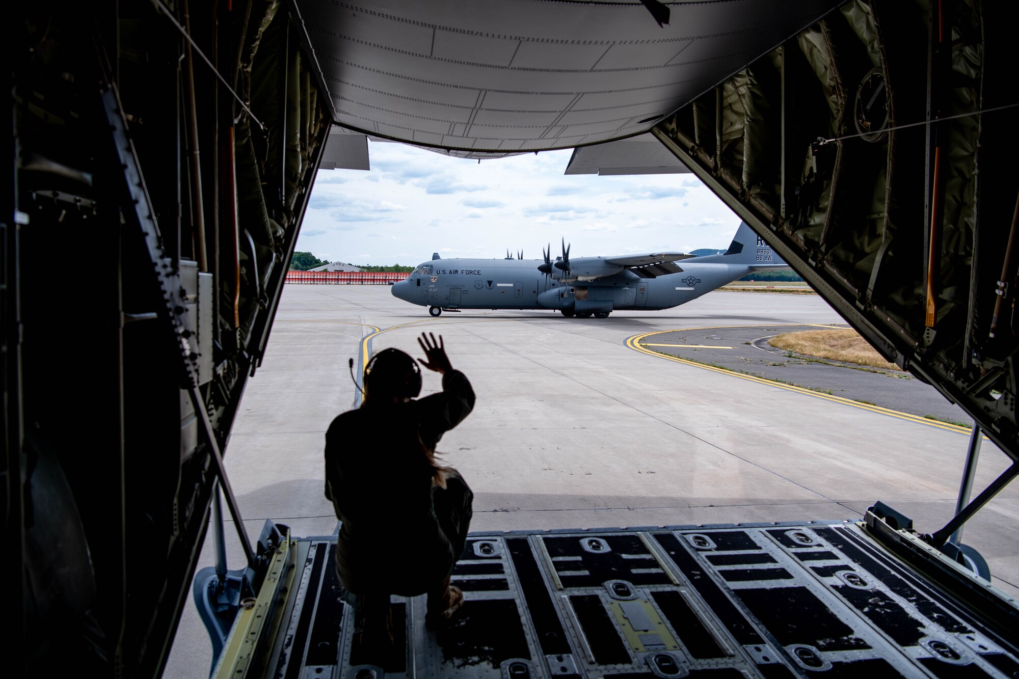 A U.S. Air Force Master Sgt. Alexandra White, U.S. Air Forces in Europe - Air Forces Africa loadmaster, waves to a U.S. Air Force C-130J Super Hercules aircraft after a large formation flight at Ramstein Air Base, July 14, 2023.