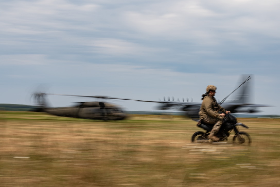 A service member rides a minibike across a field.