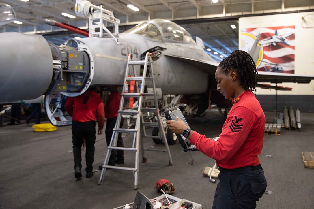 A sailor conducts routine maintenance on  an aircraft's gun.