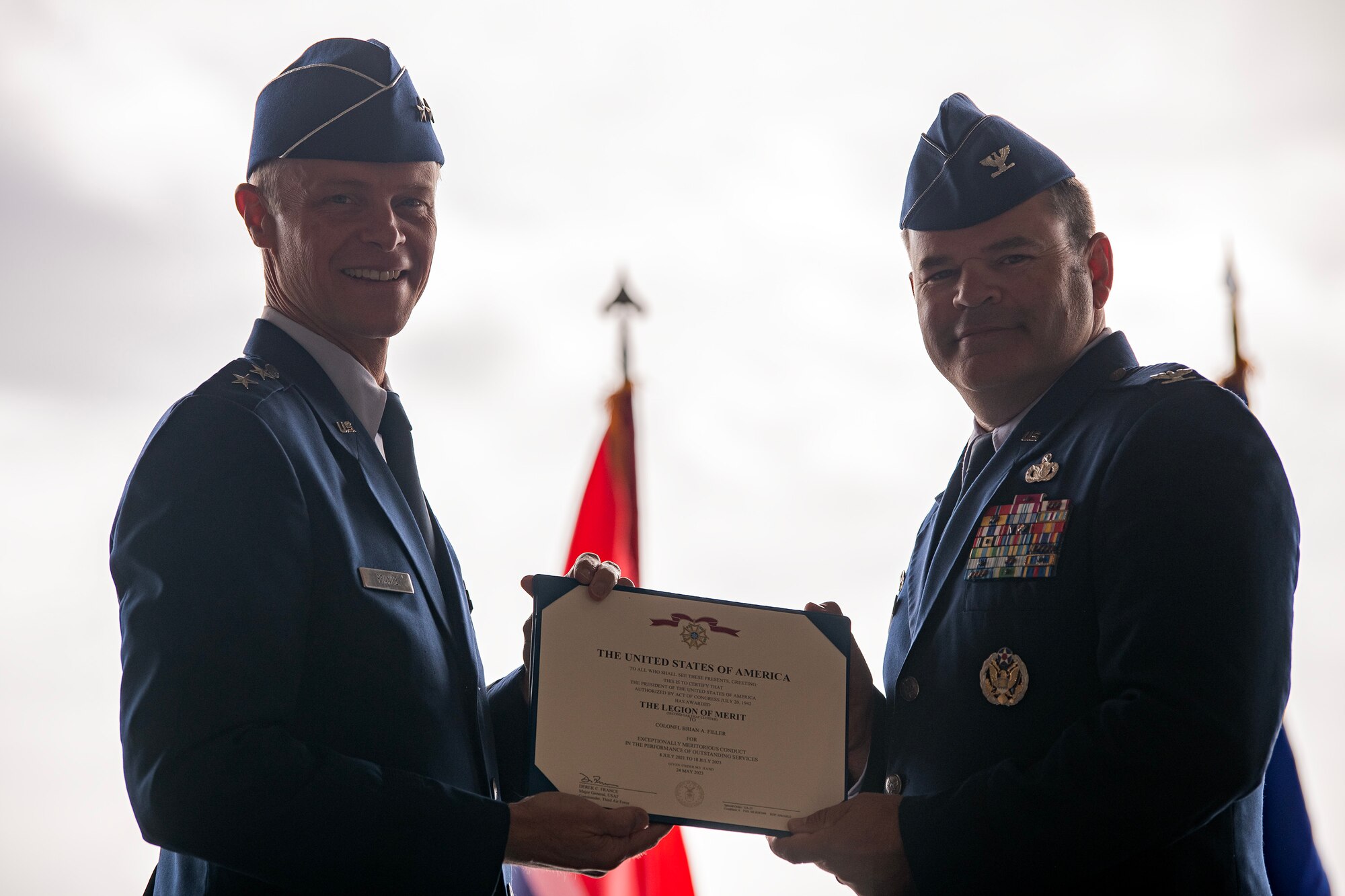 U.S. Air Force Col. Brian Filler, right, 501st Combat Support Wing outgoing commander, receives the Legion of Merit citation from Maj. Gen. Derek France, Third Air Force commander, during a change of command ceremony at RAF Fairford, England, July 18, 2023. During the ceremony Filler relinquished command of the 501st CSW to Col. Dennis Phillips. (U.S. Air Force photo by Staff Sgt. Eugene Oliver)