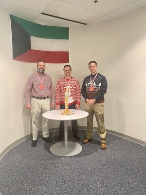 Three men posing in front of a model.